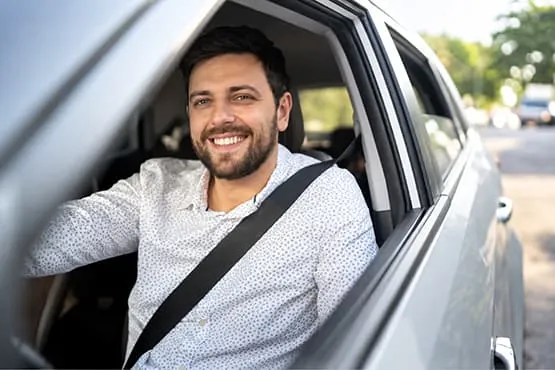 Chauffeur souriant dans une berline, visible depuis la fenêtre ouverte de la voiture.