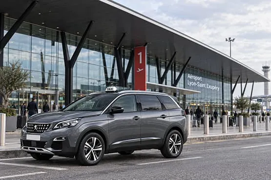 Berline grise avec enseigne taxi devant le terminal 1 de l’aéroport Lyon-Saint-Exupéry.